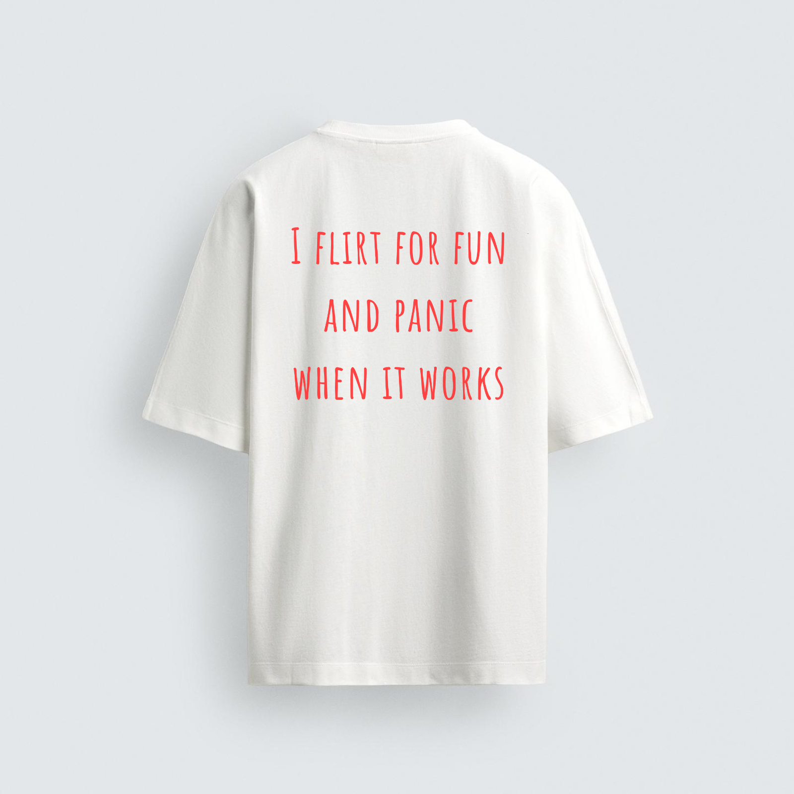 A back view of a white oversized heavyweight t-shirt featuring the humorous text "I FLIRT FOR FUN AND PANIC WHEN IT WORKS" printed in red capital letters.
