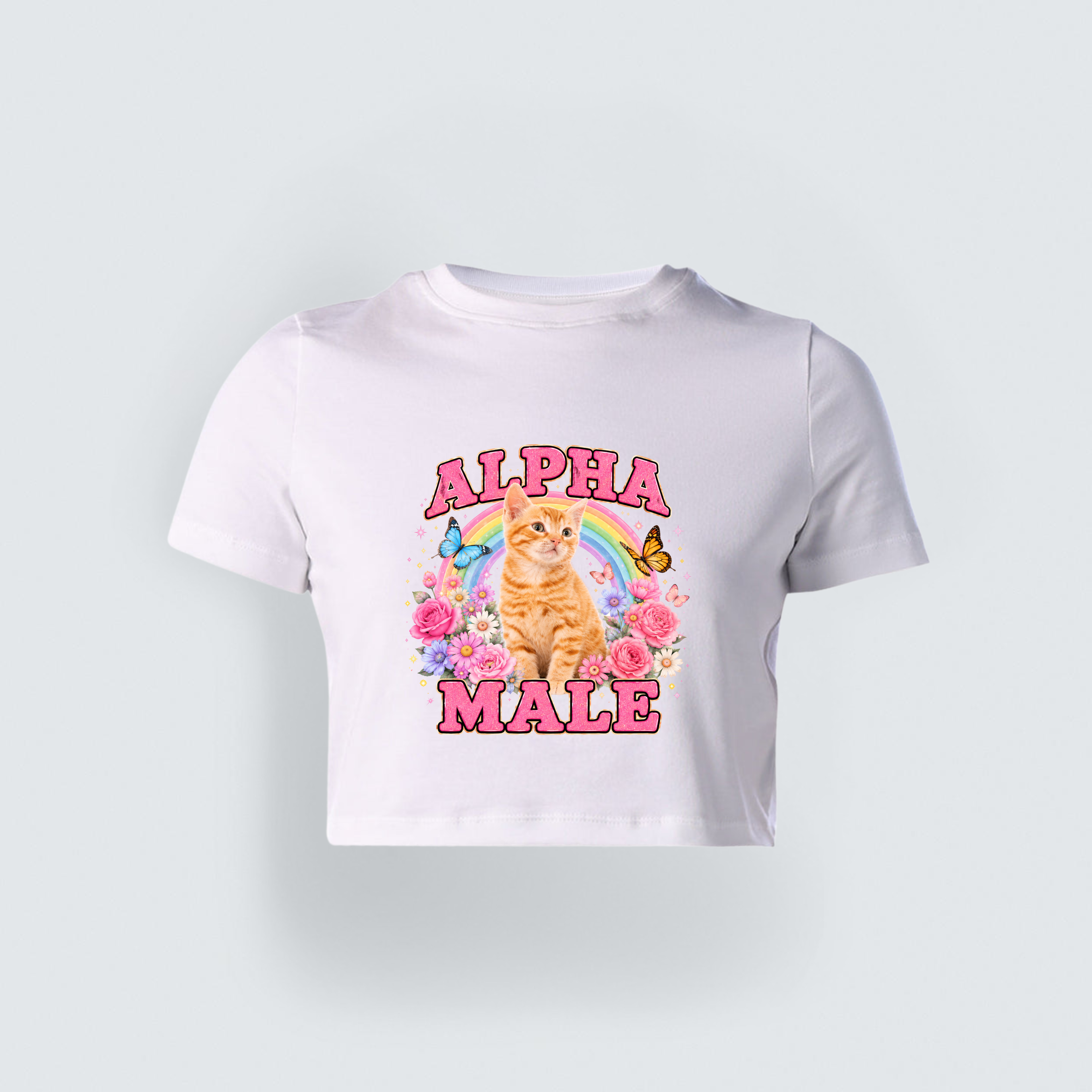 A white cropped baby tee for girls featuring a vibrant graphic of a cute orange kitten, a rainbow, flowers, and the sarcastic text Alpha Male in bold pink lettering.