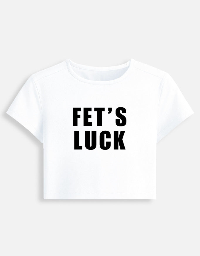 A white short-sleeved cropped baby tee featuring the text 'FET'S LUCK' printed in bold, black capital letters across the chest, displayed on a clean light gray background.