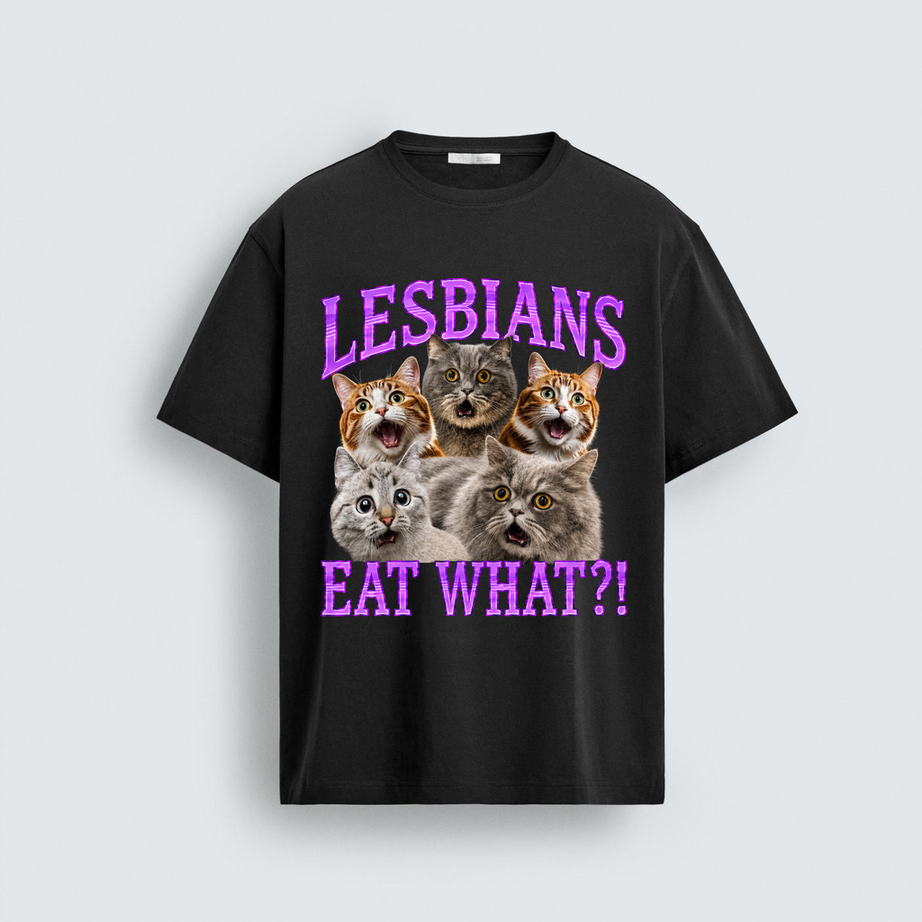 A black short-sleeve graphic t-shirt featuring five shocked cats with wide eyes and open mouths. Purple wavy text above the cats reads 'LESBIANS' and purple wavy text below reads 'EAT WHAT?!'.