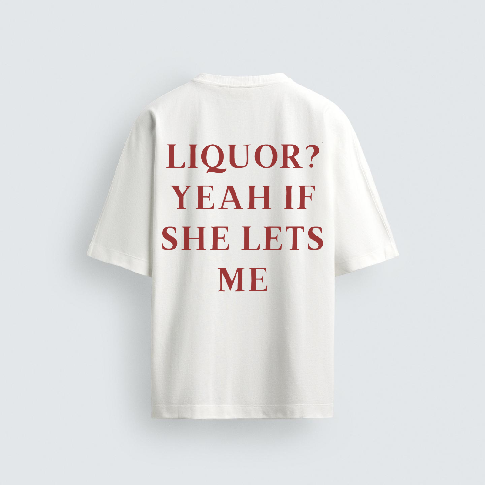 The back view of a plain white, oversized t-shirt featuring the stacked text 'LIQUOR? YEAH IF SHE LETS ME' in a dark red, serif font.