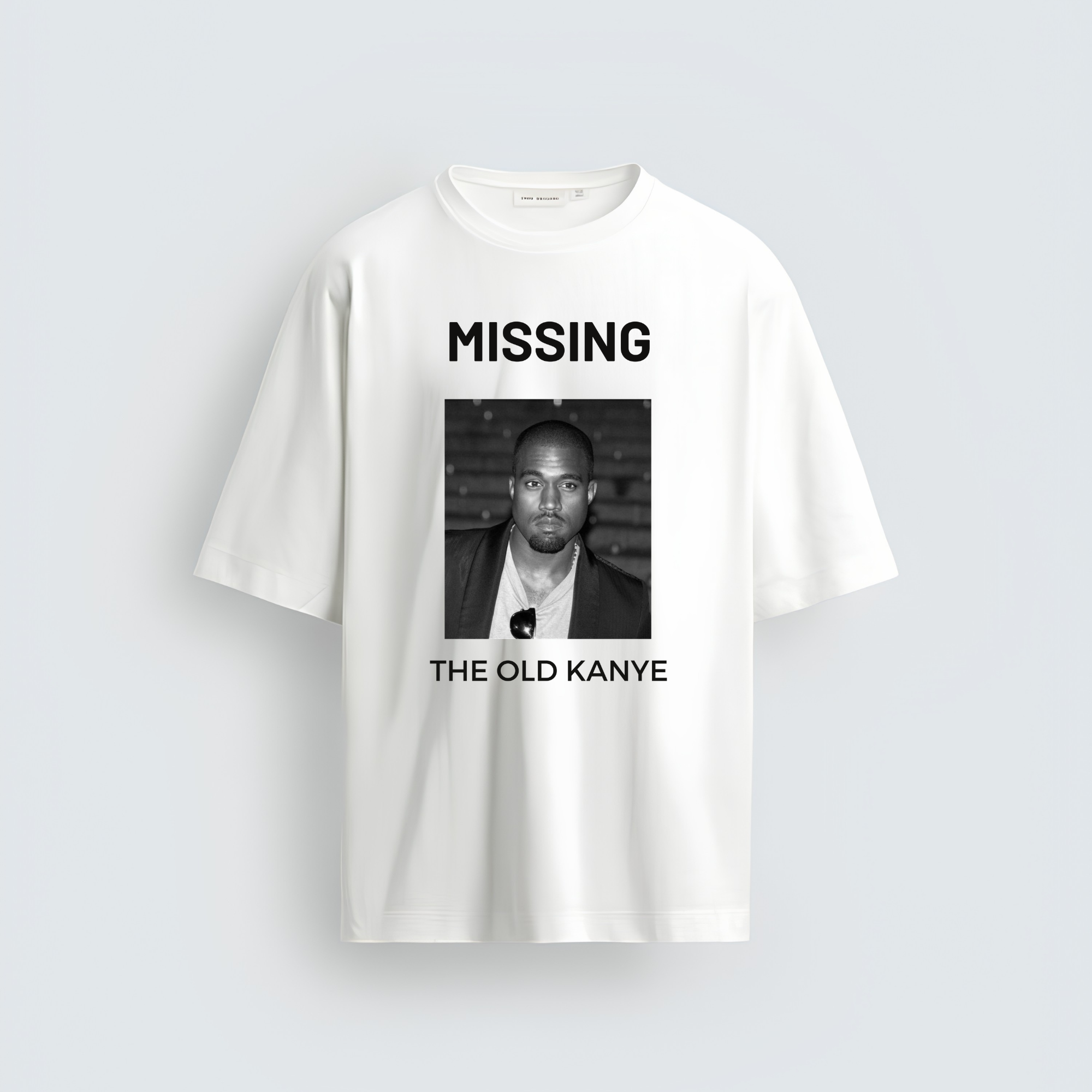 A white unisex oversized streetwear t-shirt featuring a black and white graphic on the center chest with the word "MISSING" above a portrait of Kanye West and the text "THE OLD KANYE" underneath.