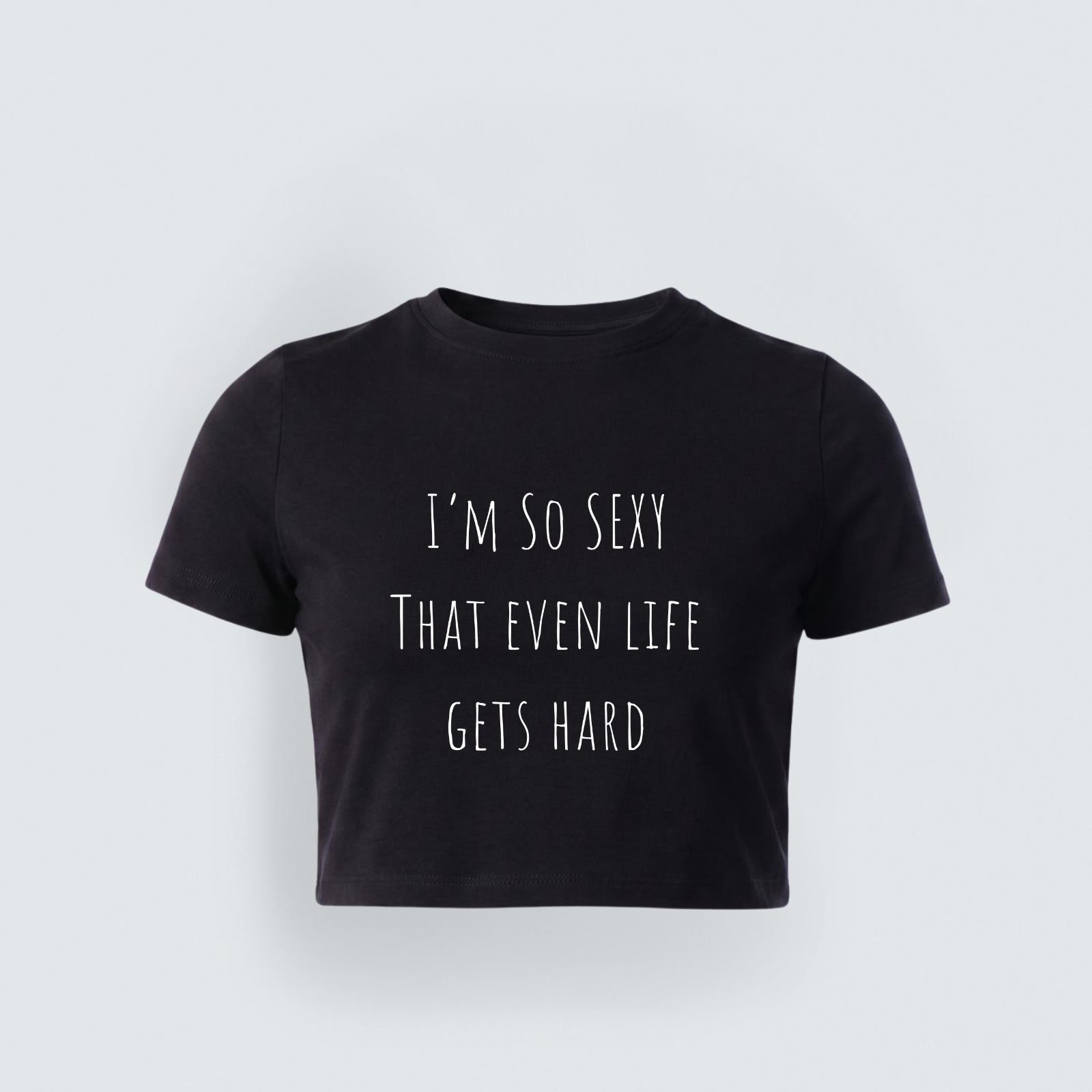 A black short-sleeved cropped baby tee featuring the text 'I'M SO SEXY THAT EVEN LIFE GETS HARD' in a thin, white, minimalist handwritten font.