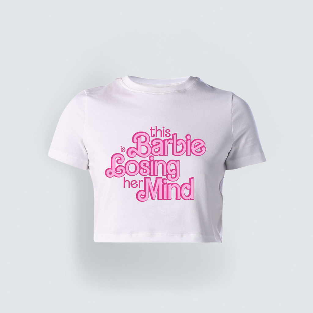 A white cropped baby tee featuring a retro pink graphic text layout on the front that reads "this Barbie is Losing her Mind."